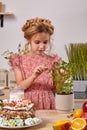 Little girl is making a homemade cake with an easy recipe at kitchen against a white wall with shelves on it. Royalty Free Stock Photo