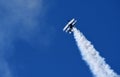 Pitts Model 12 stunt byplane with smoke trail and blue sky.