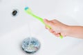 Little hand of small healthy child holding green toothbrush under fresh stream of water in white bathroom during morning health