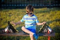 Little handsome boy in roller-blades sits in bench in summer park