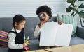 Little happy African black boy and caucasian sweet girl wearing casual sweaters, smiling, sitting together in living room at home Royalty Free Stock Photo