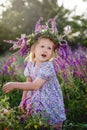 A little happy blonde girl in a sage wreath and a colorful dress in a summer blooming field