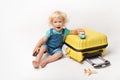 Little Happy Caucasian curly girl in comfortable denim clothes child sitting on yellow suitcase. tourist in shirt with plain And
