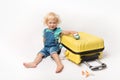 Little Happy Caucasian curly girl in comfortable denim clothes child sitting on yellow suitcase. tourist in shirt with plain And