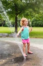 Little Children Playing At Water Splash Pad Fountain In Park Playground On Hot Summer Day