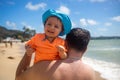 Little happy cute baby boy sitting on his dad shoulder on the background of the beach and blue sea Royalty Free Stock Photo