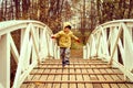 Little happy four year old kid boy in autumn clothes runs and jumps on the humpback wooden bridge in the fall park.