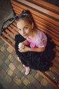 Little girl with big beautiful eyes in a fluffy skirt pack licks a horn with ice cream sitting on a wooden bench Royalty Free Stock Photo