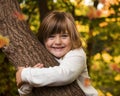 Little happy Girl hugging a tree with golden Fall Foliage in the Background
