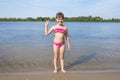 A little happy girl in a pink bathing suit standing on the bank of a river on a sunny summer day.  Beach season Royalty Free Stock Photo