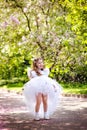 A little happy girl plays under a blooming apple tree. The child throws the petals of pink flowers. Summer fun for families with Royalty Free Stock Photo