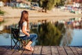 Little happy girl sitting on a wooden pier with fishing rod