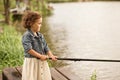 Little happy girl in the village fishing with rod. Summer country life.