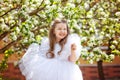 A little happy girl in a white dress is dancing under a blooming apple tree with flowers. Summer fun for families with children in Royalty Free Stock Photo