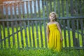 Little happy girl in yellow dress near the wooden fence in the village.