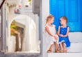 Little happy girls in dresses at street of typical greek traditional village with white walls and colorful doors on Royalty Free Stock Photo
