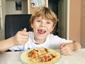 Little happy school boy eating pasta noodles and spaghetti. Cute child with tooth gap in domestic home kitchen, having