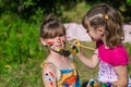 Little happy sisters play with colors in the park, children play, children paint each other Royalty Free Stock Photo