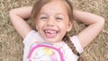 Little Happy toothless and Smiling Child Girl Laying on Yellow Lawn Dry Grass Hay in Park. Summer Time, Nature, Dreams Royalty Free Stock Photo