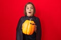 Little hispanic boy wearing a cape and holding halloween pumpkin surprised with an idea or question pointing finger with happy Royalty Free Stock Photo