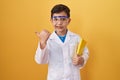 Little hispanic boy wearing scientist glasses pointing thumb up to the side smiling happy with open mouth