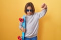 Little hispanic boy wearing sunglasses holding skate with angry face, negative sign showing dislike with thumbs down, rejection Royalty Free Stock Photo