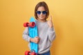 Little hispanic boy wearing sunglasses holding skate surprised with an idea or question pointing finger with happy face, number Royalty Free Stock Photo