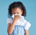 Little hispanic girl blowing her nose with tissue against blue studio background. Child feeling sick with flu virus or Royalty Free Stock Photo