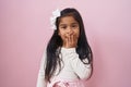 Little hispanic girl standing over pink background covering mouth with hand, shocked and afraid for mistake Royalty Free Stock Photo