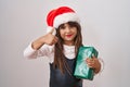 Little hispanic girl wearing christmas hat and holding gifts smiling happy and positive, thumb up doing excellent and approval Royalty Free Stock Photo