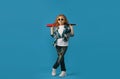 a little hooligan girl in torn jeans with a baseball bat in her hands on an isolated blue background.
