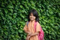 Little Indonesian schoolgirl walks with a school bag against a background of a wall with plants