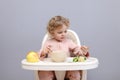 Little infant baby girl eating healthy food while sitting in high chair isolated over gray background taking broccoli having Royalty Free Stock Photo