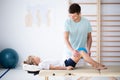 Little injure girl on massage table exercising with young male doctor