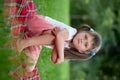 Little irritated girl sitting on plaid in grass