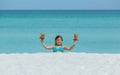 Little joyful smiling girl sitting at white sand tropical beach