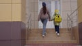 a little kid with a backpack goes with his mother hand in hand to school. little kid and mom rush to the school lesson