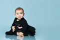 Little kid in black bodysuit with pink bow, poofy skirt and socks. She smiling, sitting on blue background. Close up, copy space