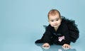 Little kid in black bodysuit with pink bow, poofy skirt and socks. She smiling, sitting on blue background. Close up, copy space