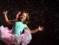 Little kid in blue t-shirt and poofy skirt. Smiling, closed eyes, jumping up against black background, pink backlight. Close up Royalty Free Stock Photo