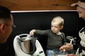 Little kid boy assistant, help to cook with mother and father in kitchen. Mixing by spoon ingredients in food processor