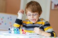 Little kid boy drawing with colorful watercolors indoors