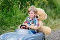 Little kid boy driving big toy car with a bear, outdoors. Royalty Free Stock Photo