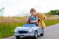 Little kid boy driving big toy car with a bear, outdoors. Royalty Free Stock Photo