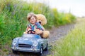 Little kid boy driving big toy car with a bear, outdoors. Royalty Free Stock Photo