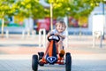 Little kid boy driving pedal race car in summer