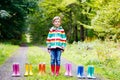 Little kid boy and group of colorful rain boots. Blond child standing in autumn forest. Close-up of schoolkid and