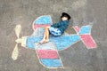 Little kid boy having fun with with airplane picture drawing with colorful chalks on asphalt. Child painting with chalk