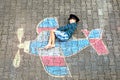 Little kid boy having fun with with airplane picture drawing with colorful chalks on asphalt. Child painting with chalk