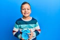 Little kid boy holding alarm clock looking positive and happy standing and smiling with a confident smile showing teeth Royalty Free Stock Photo